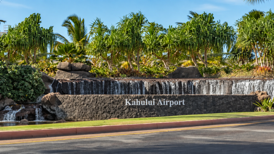 Kahului Airport entrance sign beneath a waterfall and tropical palms