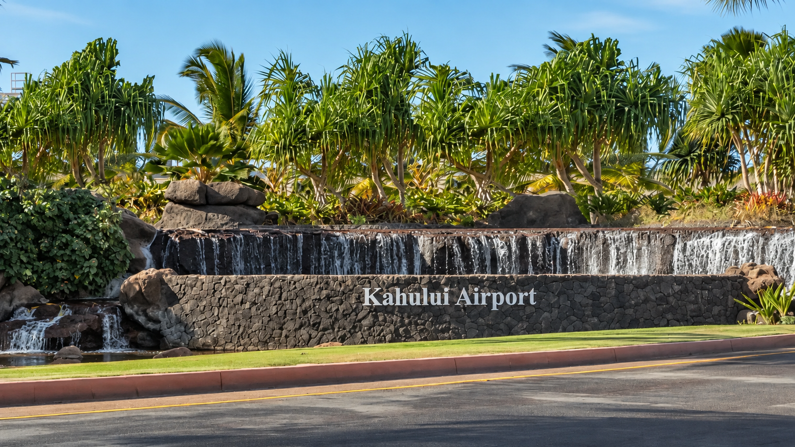 Kahului Airport entrance sign beneath a waterfall and tropical palms