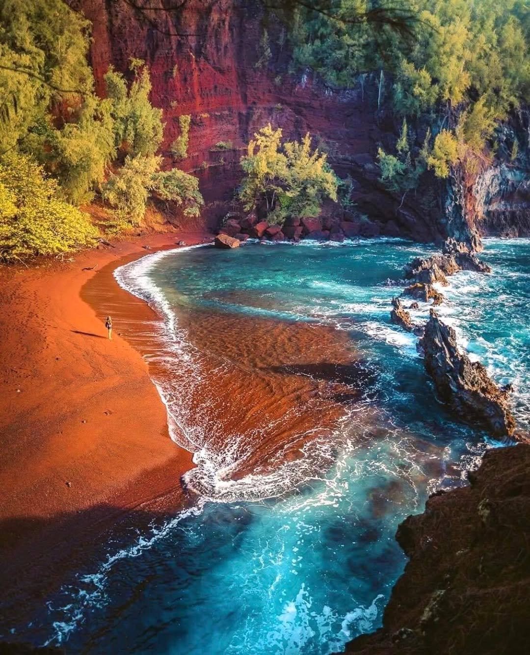 Red sand curves around Kaihalulu’s turquoise cove beneath steep red cliffs